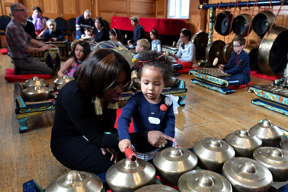 A black women, with glasses, teaching a young black girl to interact with musical instruments.